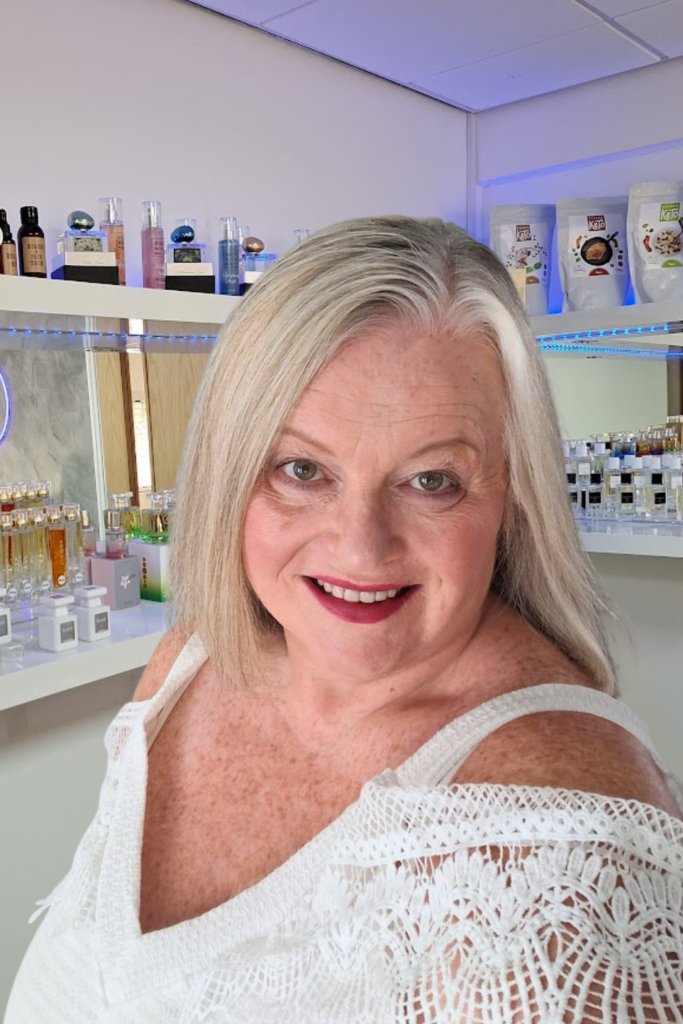 Louise Antoine, Essens Platinum Manager, smiling in front of a display of Essens perfumes and wellness products.